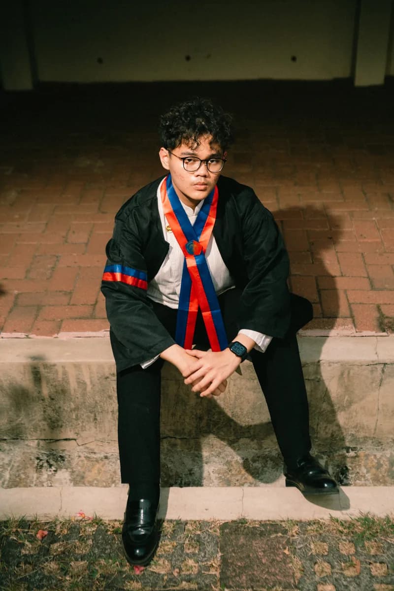 Wahyu sitting outdoors in graduation attire at night