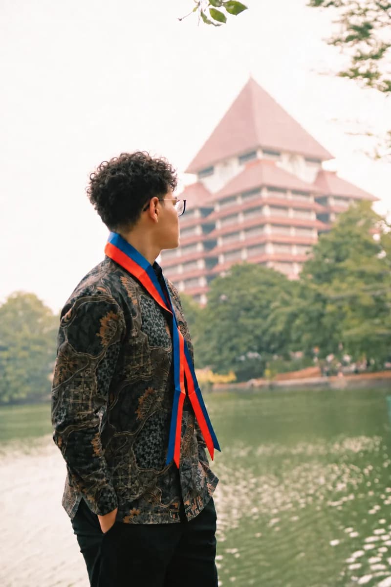 Wahyu in graduation attire near the Universitas Indonesia rectorate