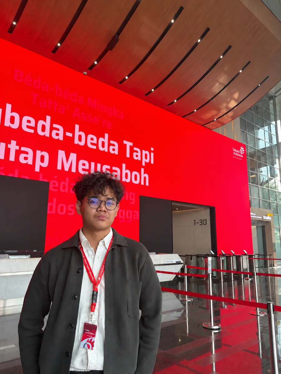 Wahyu standing in front of a red Telkom Indonesia display