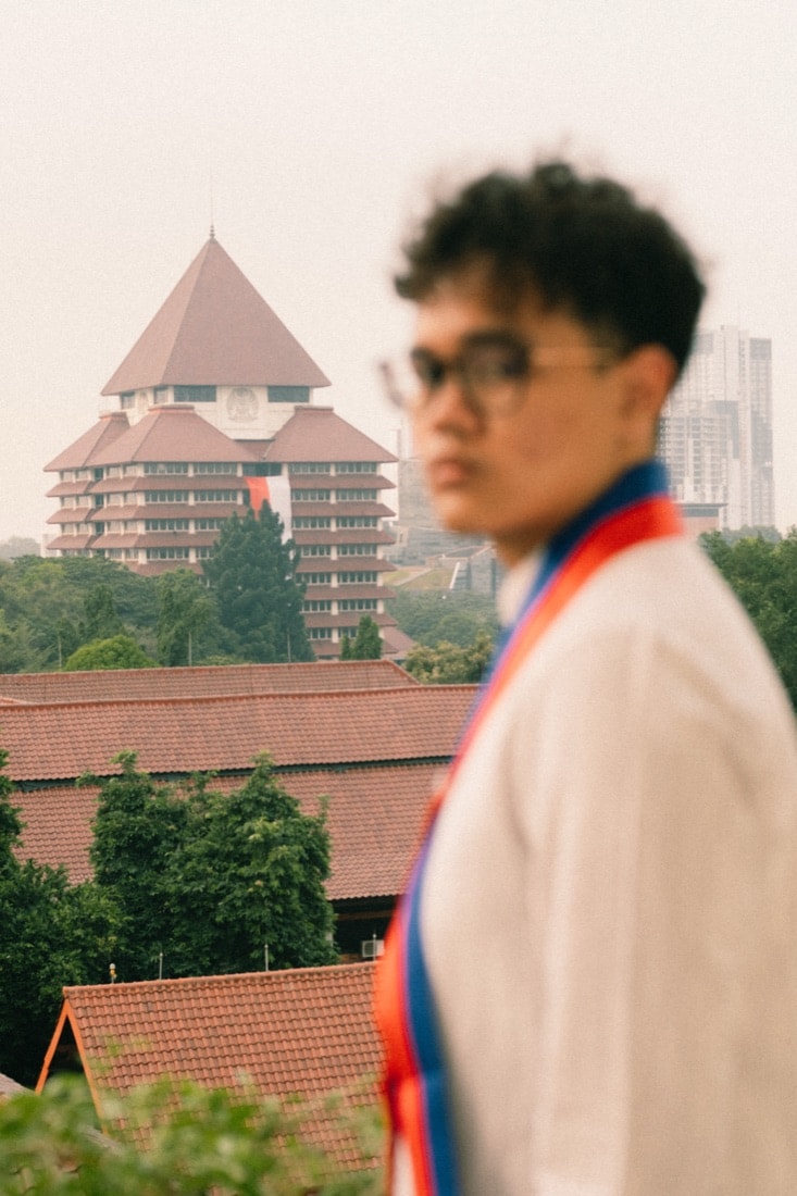 Wahyu in his graduation sash with the Universitas Indonesia rectorate behind him